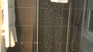 A glass-enclosed shower stall with a tiled wall and a white towel hanging on the door.