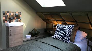 Quarto com claraboia, cama com travesseiro estampado com padrão de zebra, mesa de cabeceira, armário e pia fixa na parede.