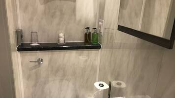 A bathroom with a marble wall, a black countertop, a toilet, a sink, a mirror, and a shelf with toiletries.