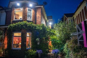 A two-story house with a brick facade, a large window, and a garden with potted plants and flowers.