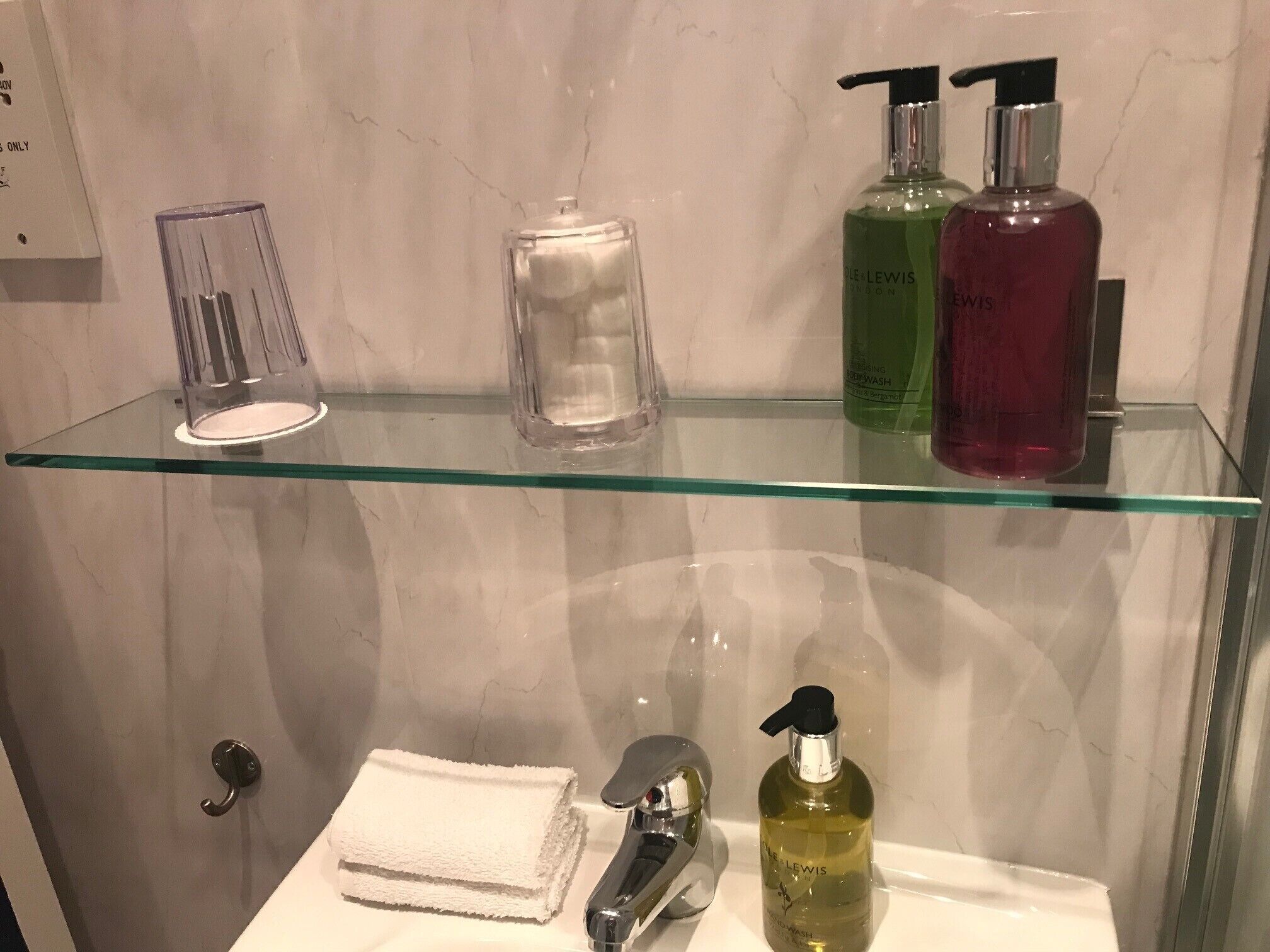 A bathroom with a glass shelf holding toiletries, a towel, and a glass container.