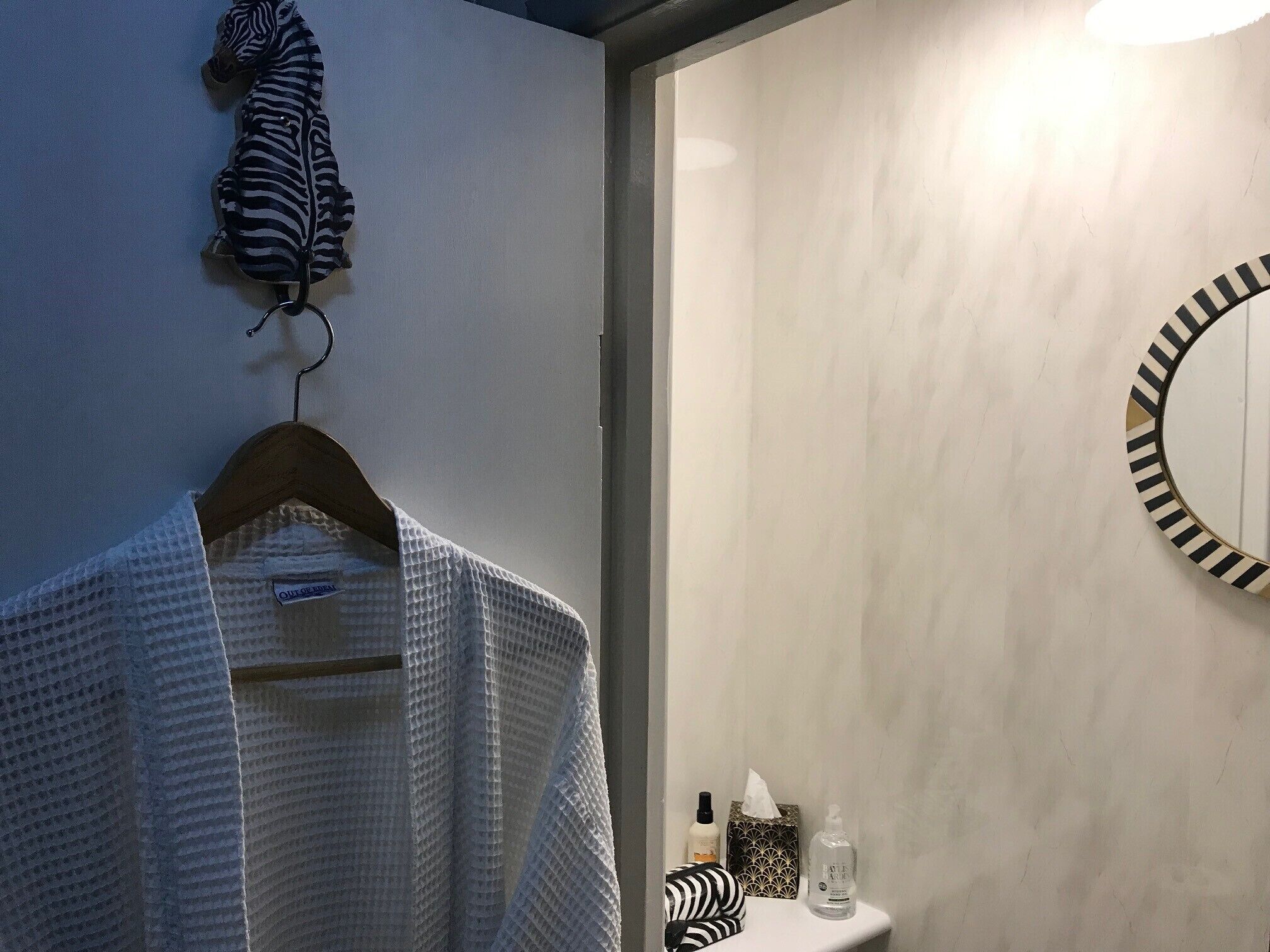 A bathroom with a towel rack holding a white towel, a mirror with a striped frame, and toiletries on the counter.