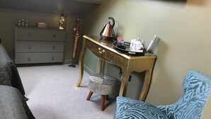 A compact living space with a grey sofa, a blue patterned ottoman, a wooden desk with a tray holding a kettle, a small table with decorative items, and a grey dresser. - Amarillo (Bournemouth)