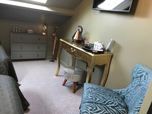 A compact living space with a grey sofa, a blue patterned ottoman, a wooden desk with a tray holding a kettle, a small table with decorative items, and a grey dresser. - Amarillo (Bournemouth)