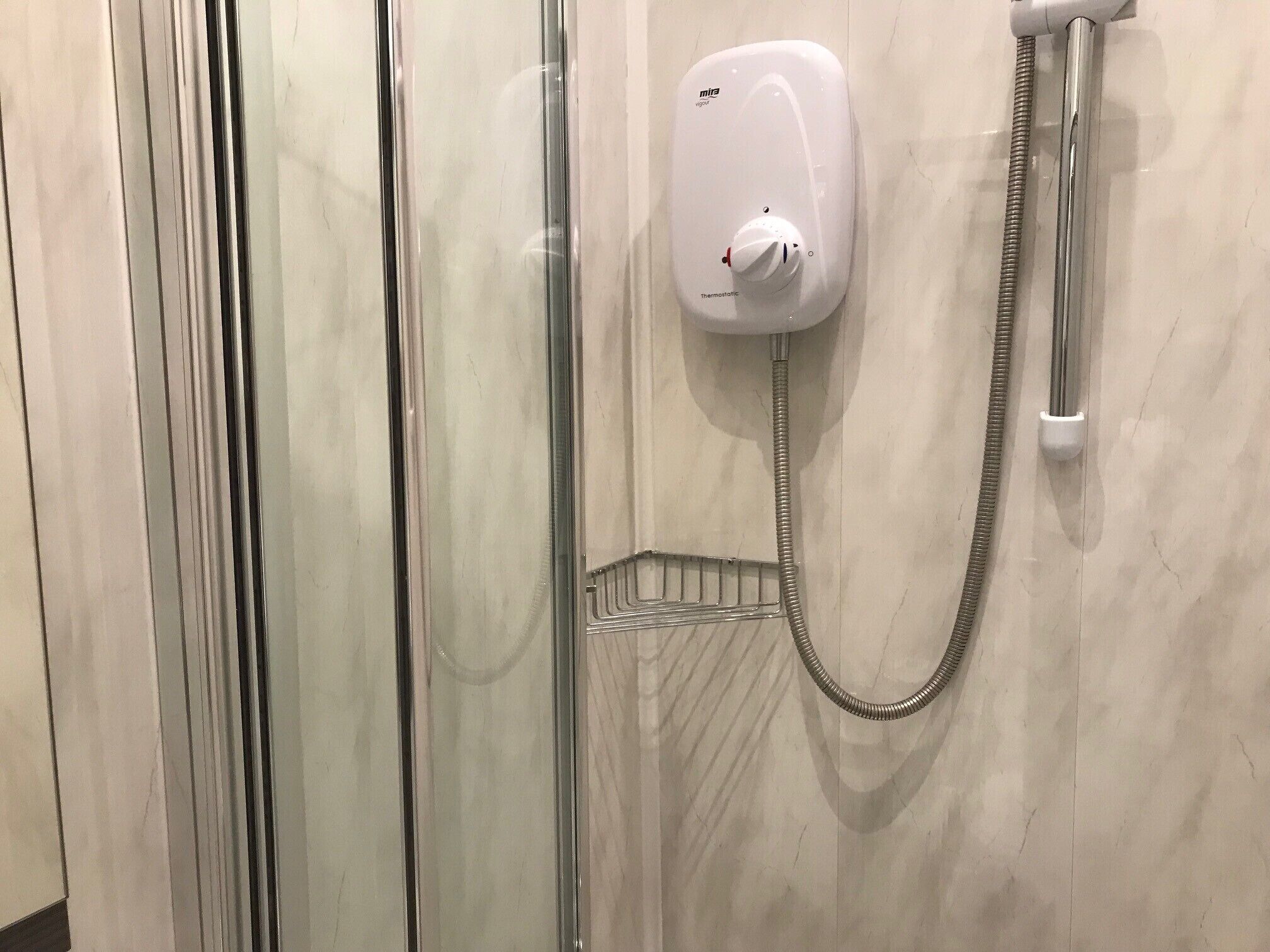 A bathroom with a glass shower enclosure, a white handheld showerhead, and a chrome shower hose.