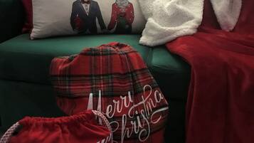 A green sofa with a white and red pillow featuring reindeer, a red plaid blanket, and a red bag with 'Merry Christmas' text.