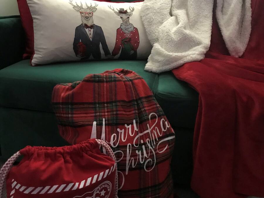 A green sofa with a white and red pillow featuring reindeer, a red plaid blanket, and a red bag with 'Merry Christmas' text.