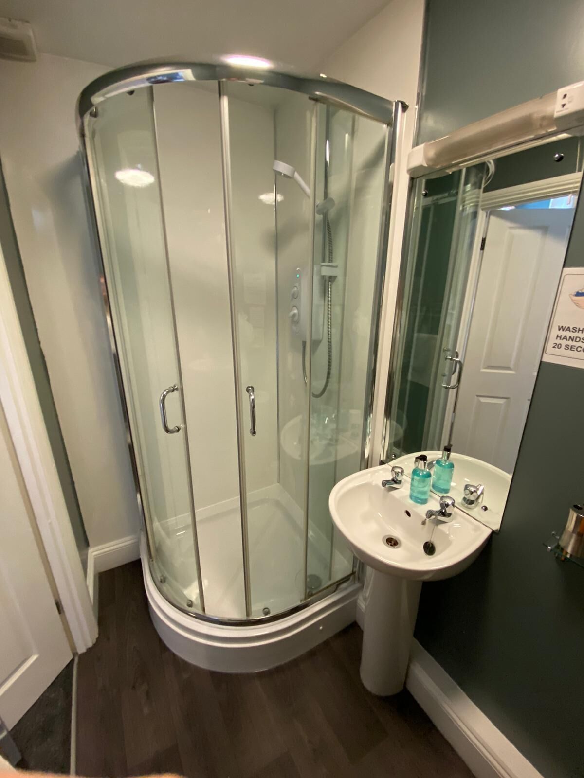 A glass-enclosed shower with a white sink and two bottles of hand soap.