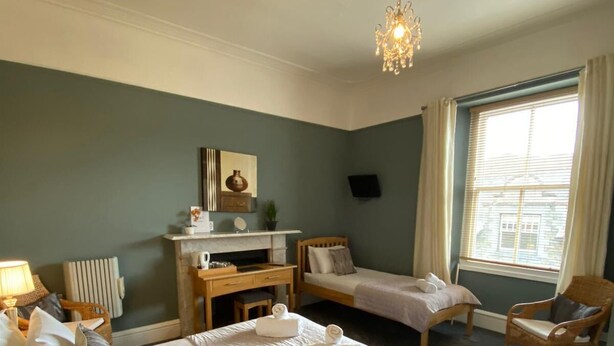 A bedroom with a large bed, bedside tables, a desk, a chair, and a window with curtains. - Ambleside Central (Ambleside)