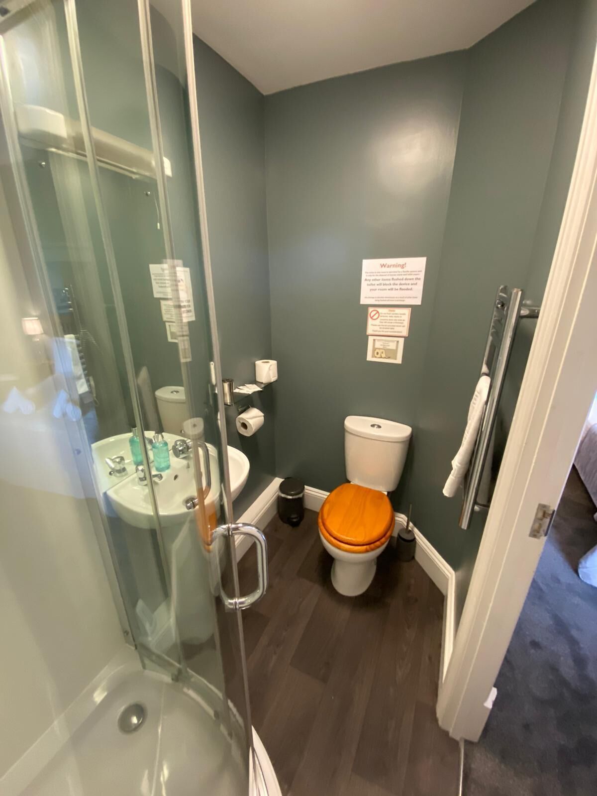 Un baño con cabina de ducha de vidrio, un lavabo con artículos de aseo, un inodoro con asiento naranja y un perchero para toallas.