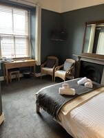 A hotel room with a bed, a desk, a chair, a television, and a fireplace.