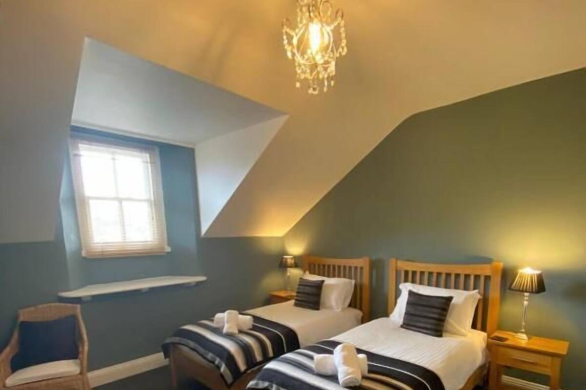 A bedroom with two beds, a chandelier, a window, and a chair.