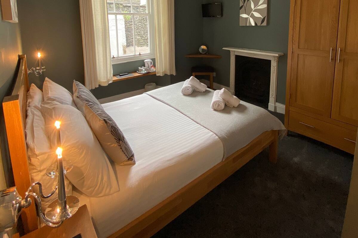 A bedroom with a bed, bedside table, lamp, window with curtains, and a fireplace.