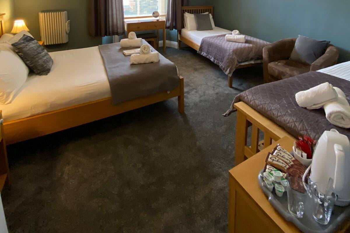 A hotel room with two beds, a desk, a chair, a radiator, and a window with curtains.