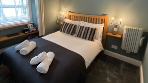 A neatly made bed with a wooden headboard, a bedside table with a lamp, and a radiator. - Ambleside Central (Ambleside)