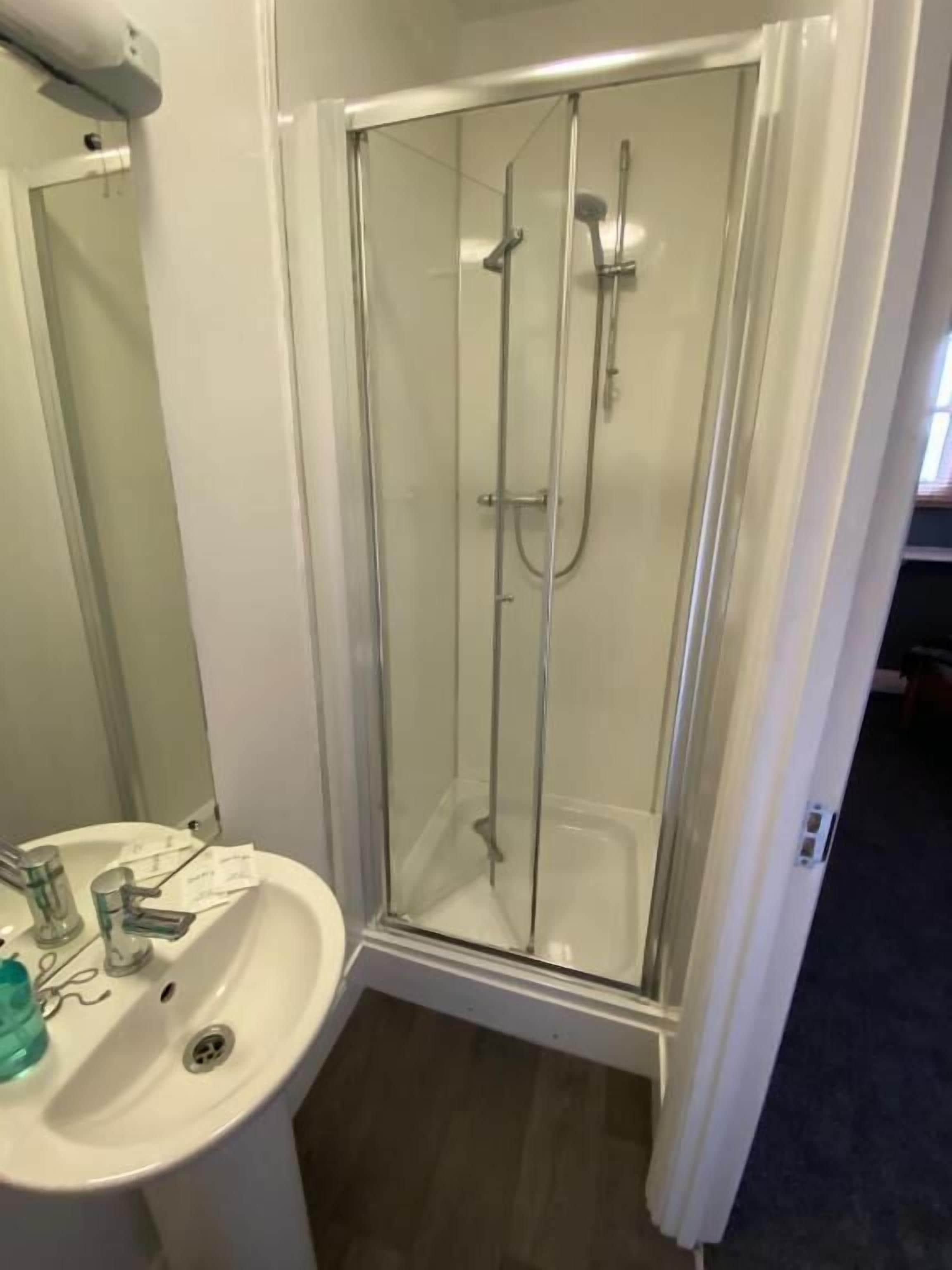 A bathroom with a glass-enclosed shower, a sink, and a mirror.