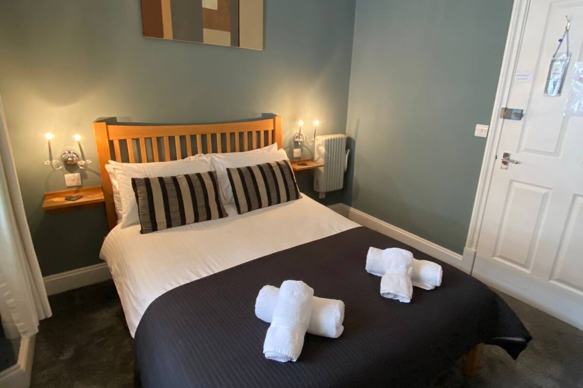 A neatly made bed with a black and white striped pillow, a wooden headboard, and a bedside table with a lamp.