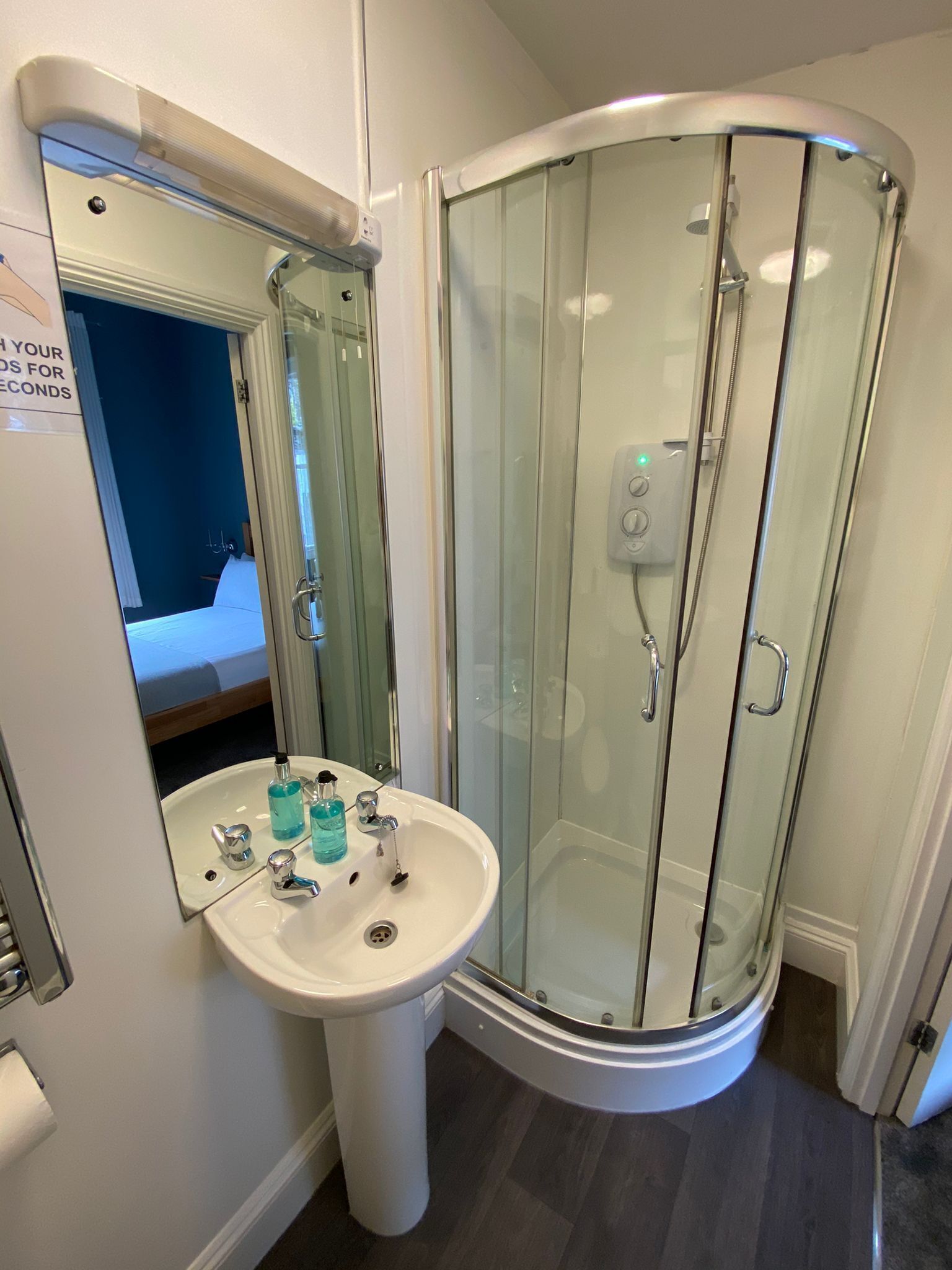 A modern bathroom with a glass-enclosed shower, a pedestal sink, and a mirror.
