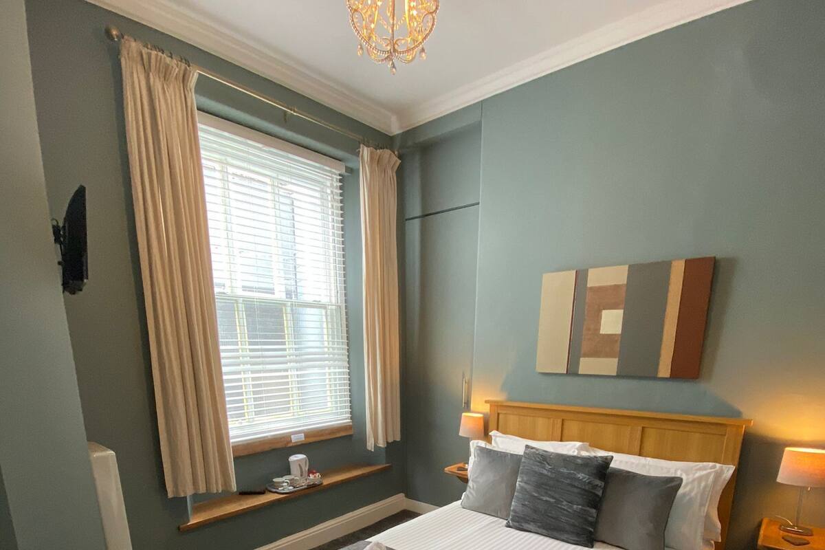 A neatly made bed with towels, a bedside table with a lamp, a window with curtains, and a chandelier.