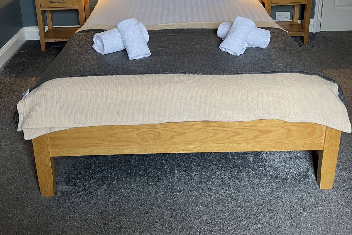 A neatly made bed with a wooden headboard, two bedside tables with lamps, and towels on the bed.