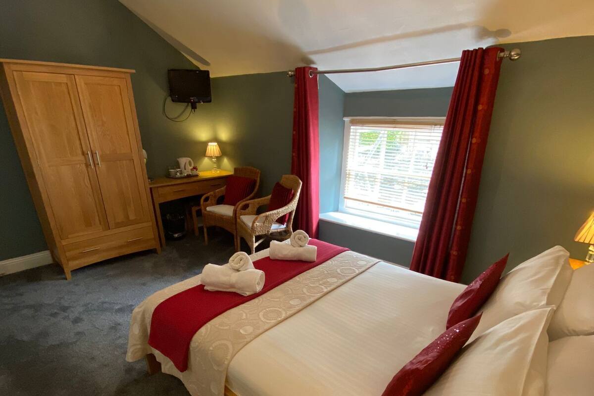 A hotel room with a bed, a desk, a chair, a wardrobe, and a window with curtains.