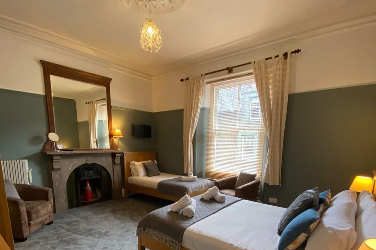 A hotel room with two beds, a fireplace, a mirror, a television, and a window with curtains.
