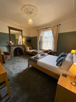 A hotel room with two beds, a fireplace, a mirror, a television, and a window with curtains.