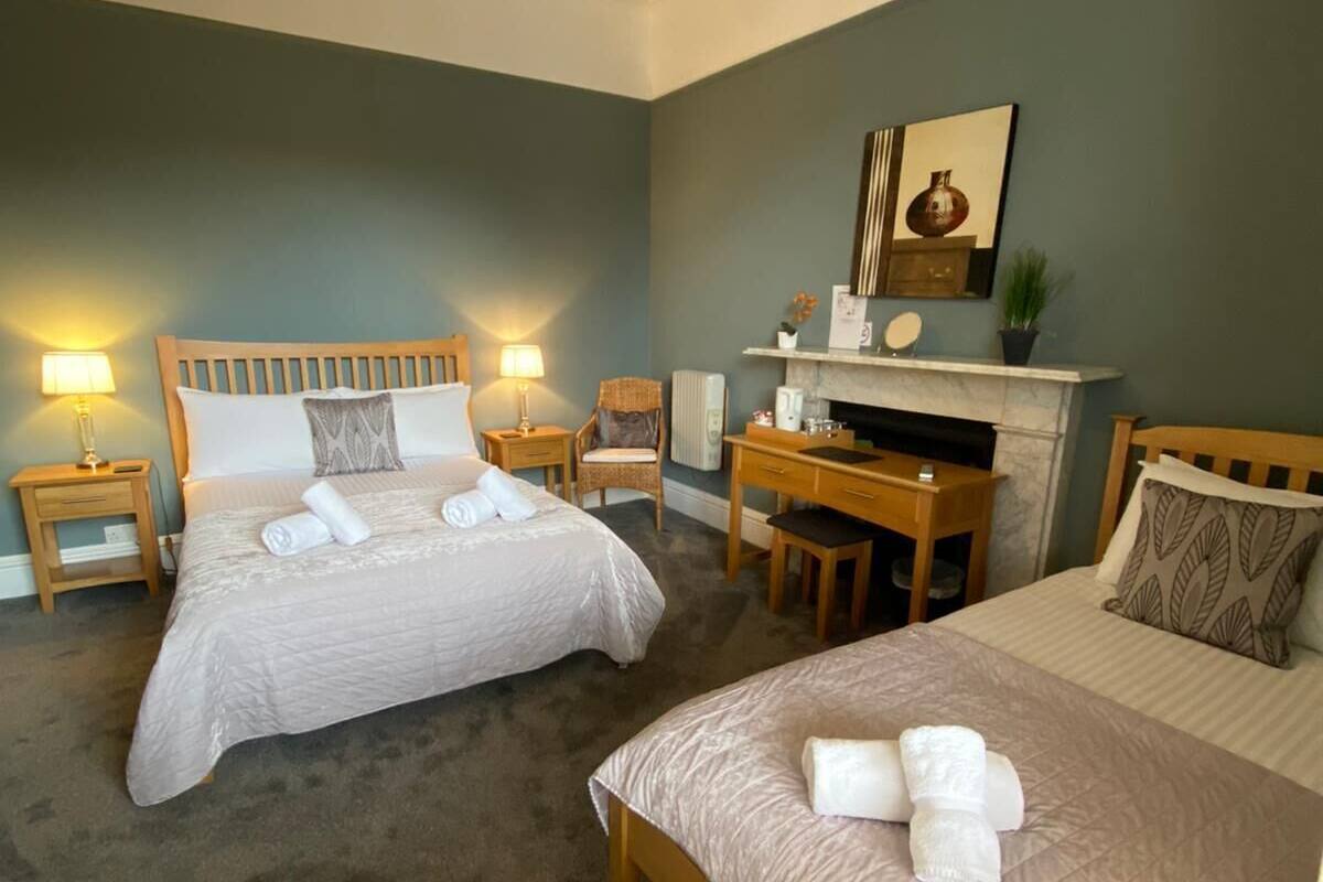 A hotel room with two beds, a desk, a chair, a fireplace, and a chandelier.
