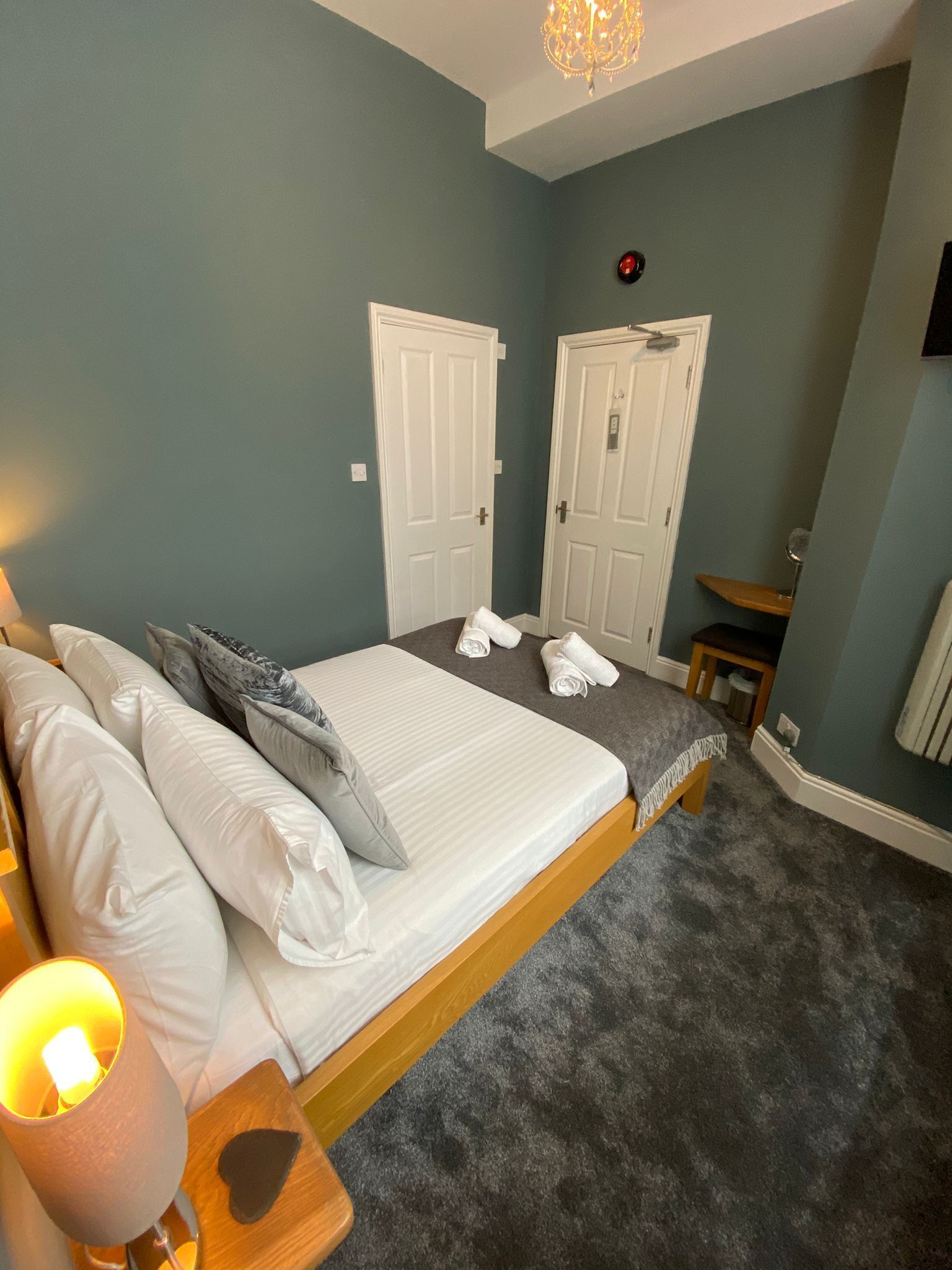 A bedroom with a bed, pillows, a bedside lamp, a chair, a small table, and two doors.