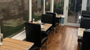 A conservatory with wooden flooring, black chairs, and tables.
