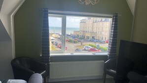 A room with a large window overlooking a parking lot and buildings. There are two armchairs and a television.