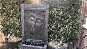 A stone fountain with a Buddha face, surrounded by potted plants and a wooden fence.