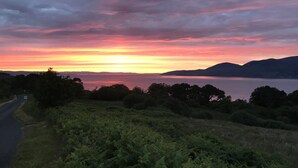 Een zonsondergang boven een meer, met bergen op de achtergrond en een weg aan de linkerkant.