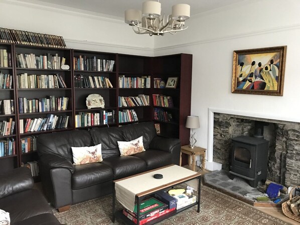 A living room with a black leather sofa, a coffee table, and a fireplace. There are bookshelves filled with books and a painting on the wall.