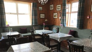 Een sfeervol restaurant met houten wanden, meerdere tafels met kleurrijke tafelkleden en een zitgedeelte met een bank.