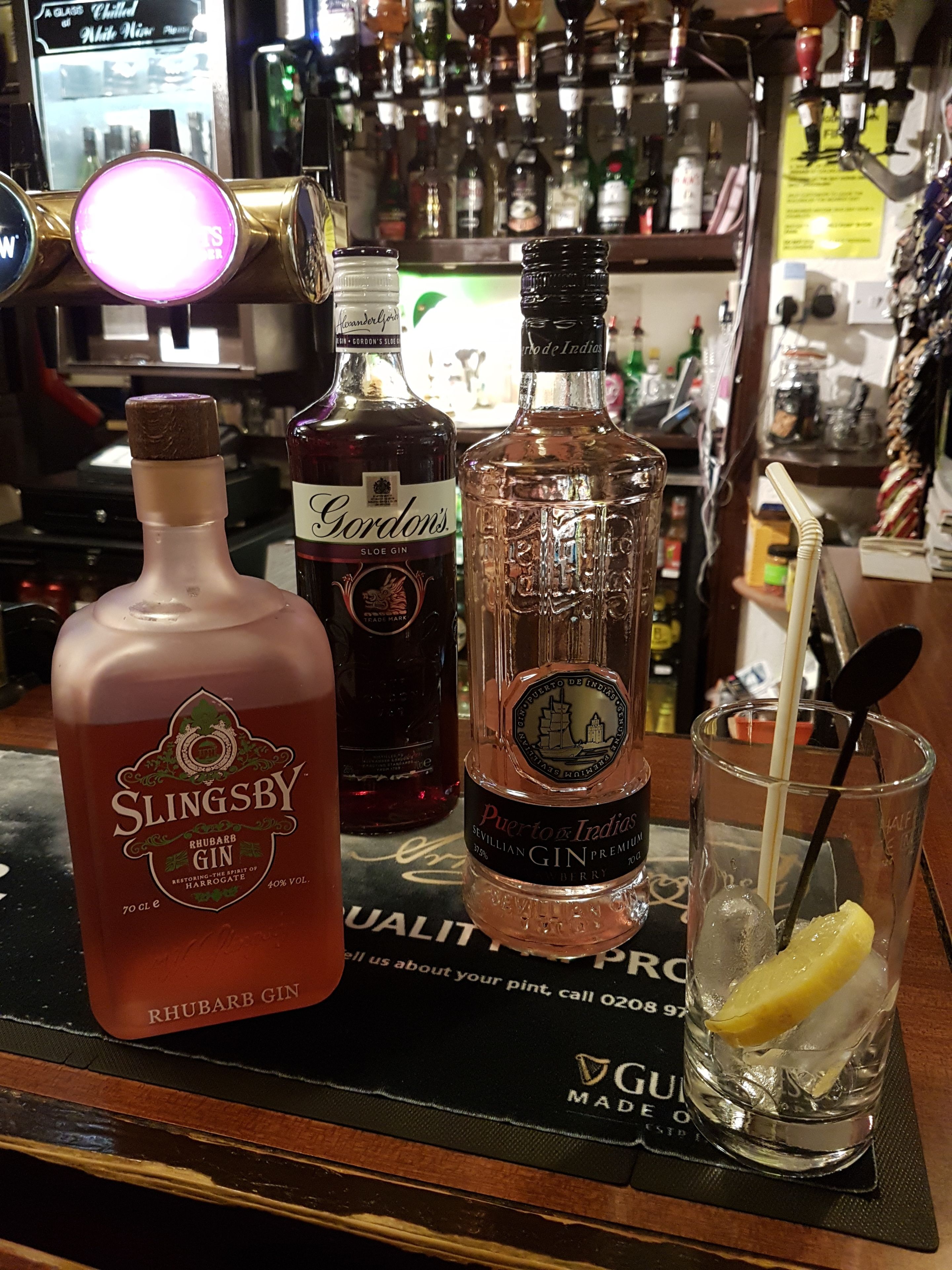 A bar counter with various bottles of gin and a glass with a lemon slice.