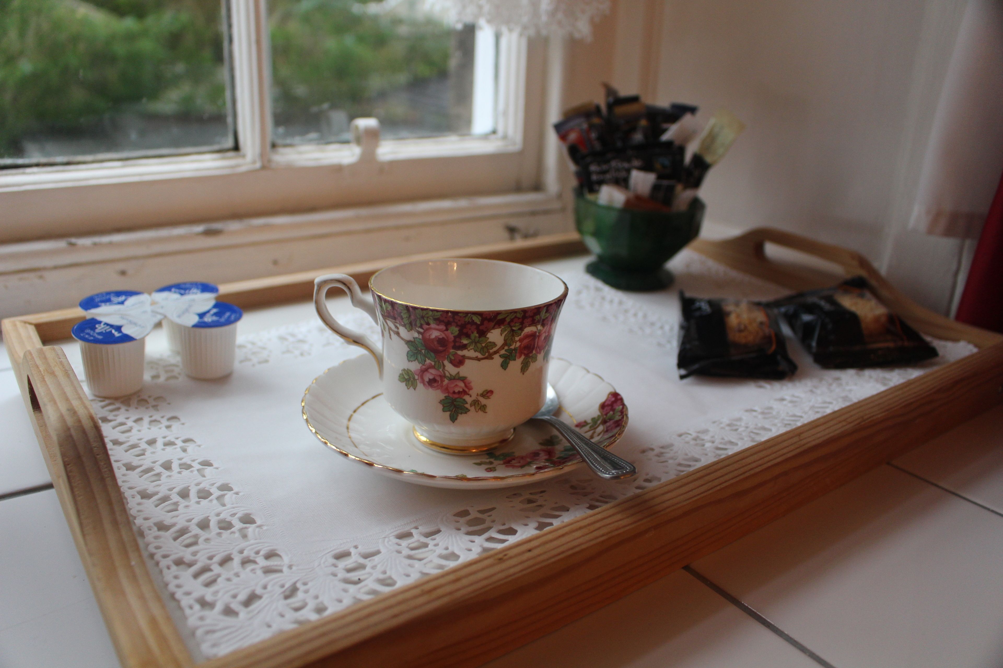 A tray with a floral cup and saucer, a spoon, and a green bowl with tea bags.