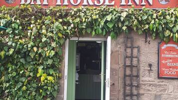 Exterior del Bay Horse Inn, con una puerta verde, muros cubiertos de hiedra y un letrero con el nombre del establecimiento.