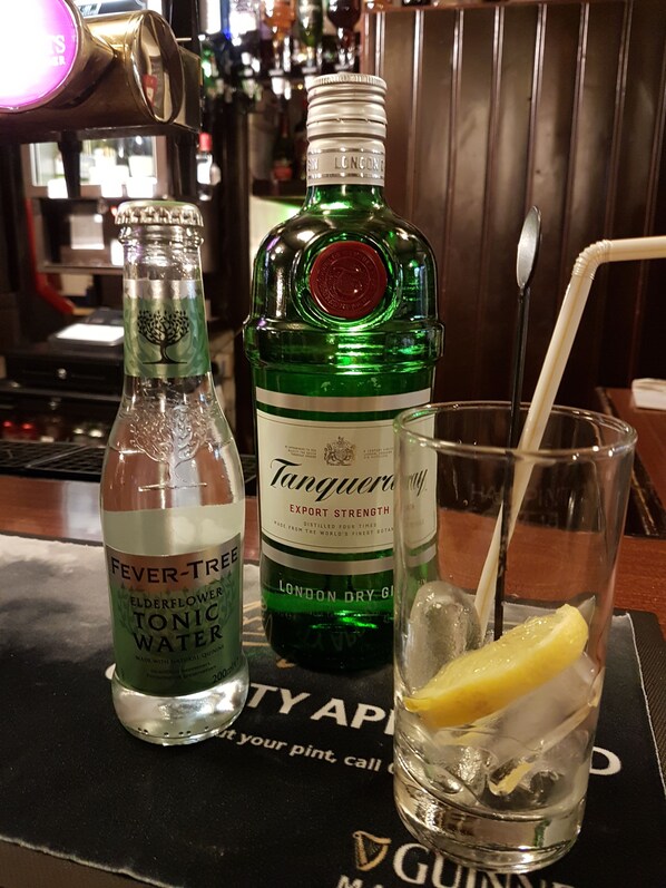 Un bar avec une bouteille d’eau tonique à la fleur de sureau de la marque Fever-Tree, une bouteille de gin Tanqueray et un verre contenant une tranche de citron et des glaçons.