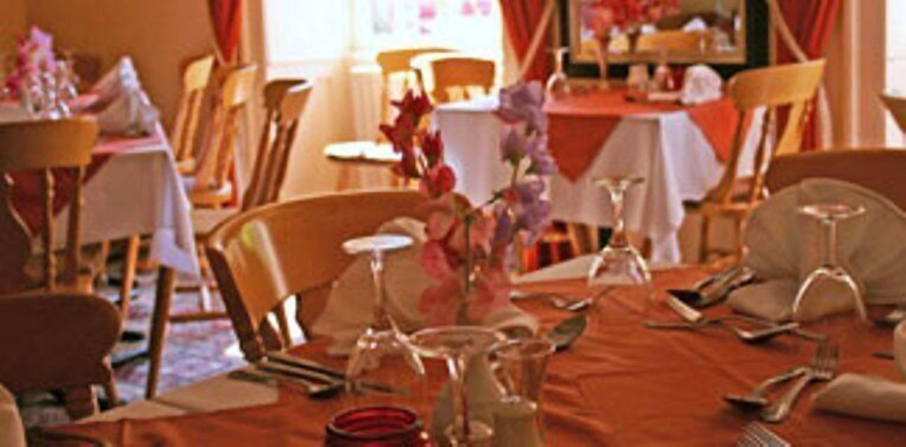 Comedor con mesas dispuestas para comer, sillas y un jarrón con flores.
