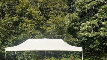 A white tent with a picnic table and chairs set up on a grassy area surrounded by trees.