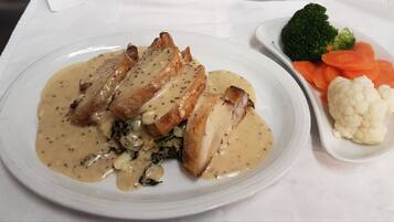 Une assiette de nourriture nappée d’une sauce crémeuse, comprenant des tranches de viande et des légumes verts, accompagnée de brocolis, de carottes et de chou-fleur.