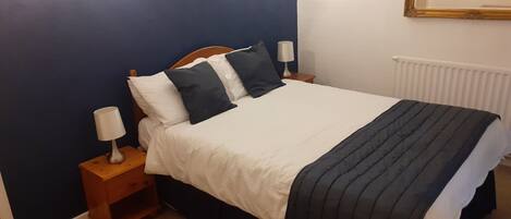Un dormitorio con una cama, mesitas de noche, una lámpara y un espejo adosado a la pared.