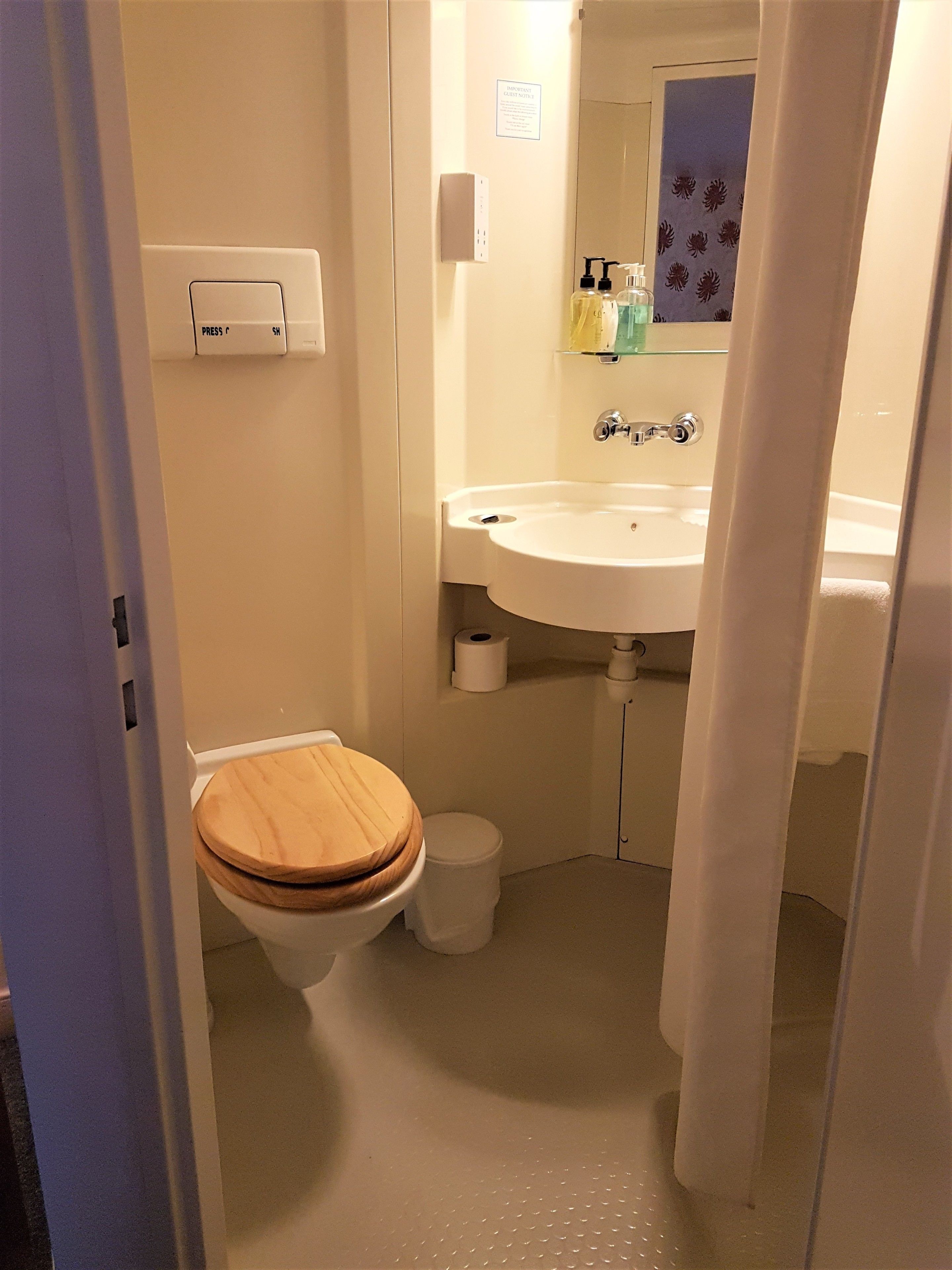 A small bathroom with a wooden toilet, a white sink, and a mirror above it.