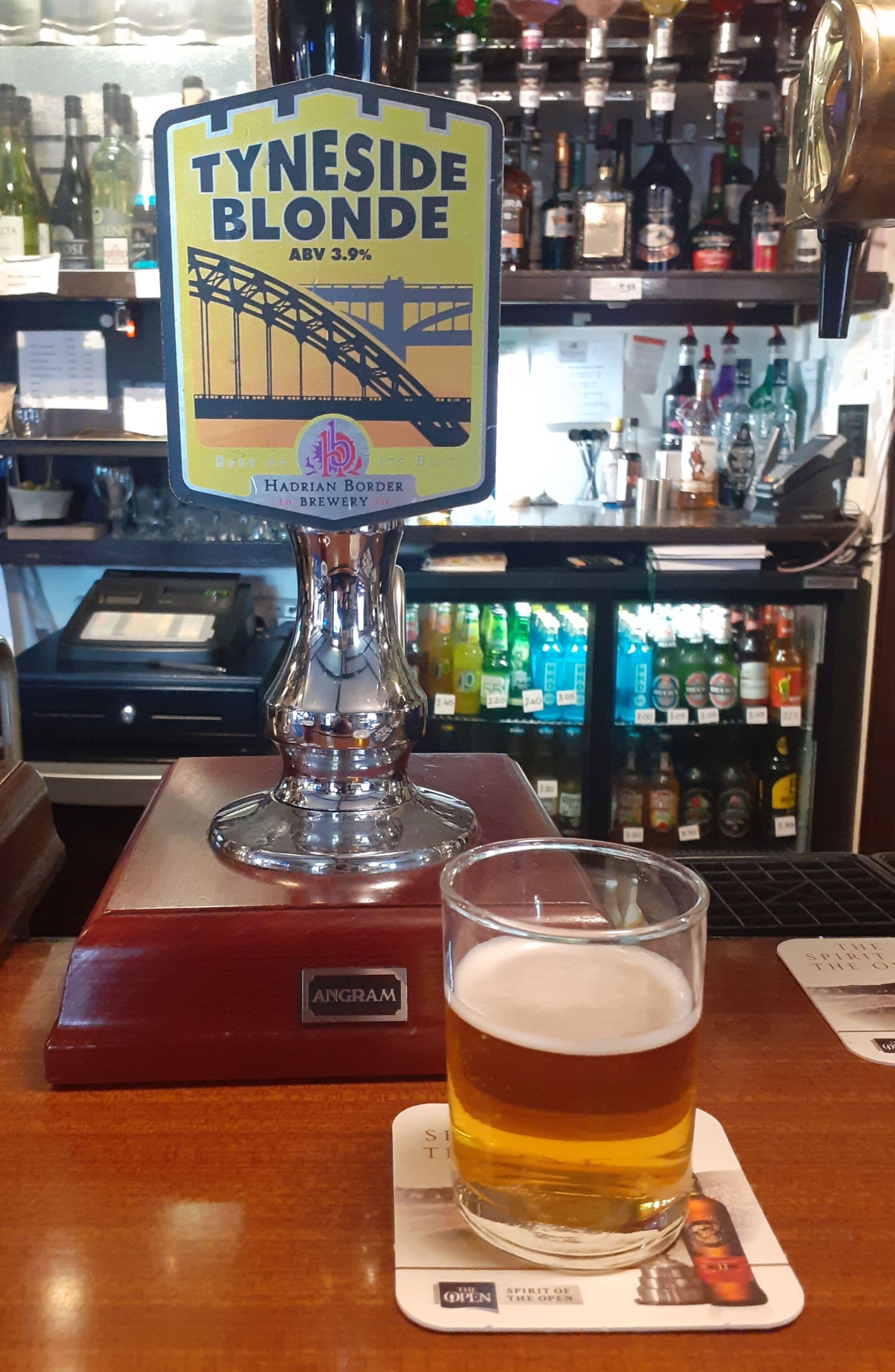 Une tireuse portant l’inscription « Tyneside Blonde » avec un verre de bière posé sur un dessous de verre.