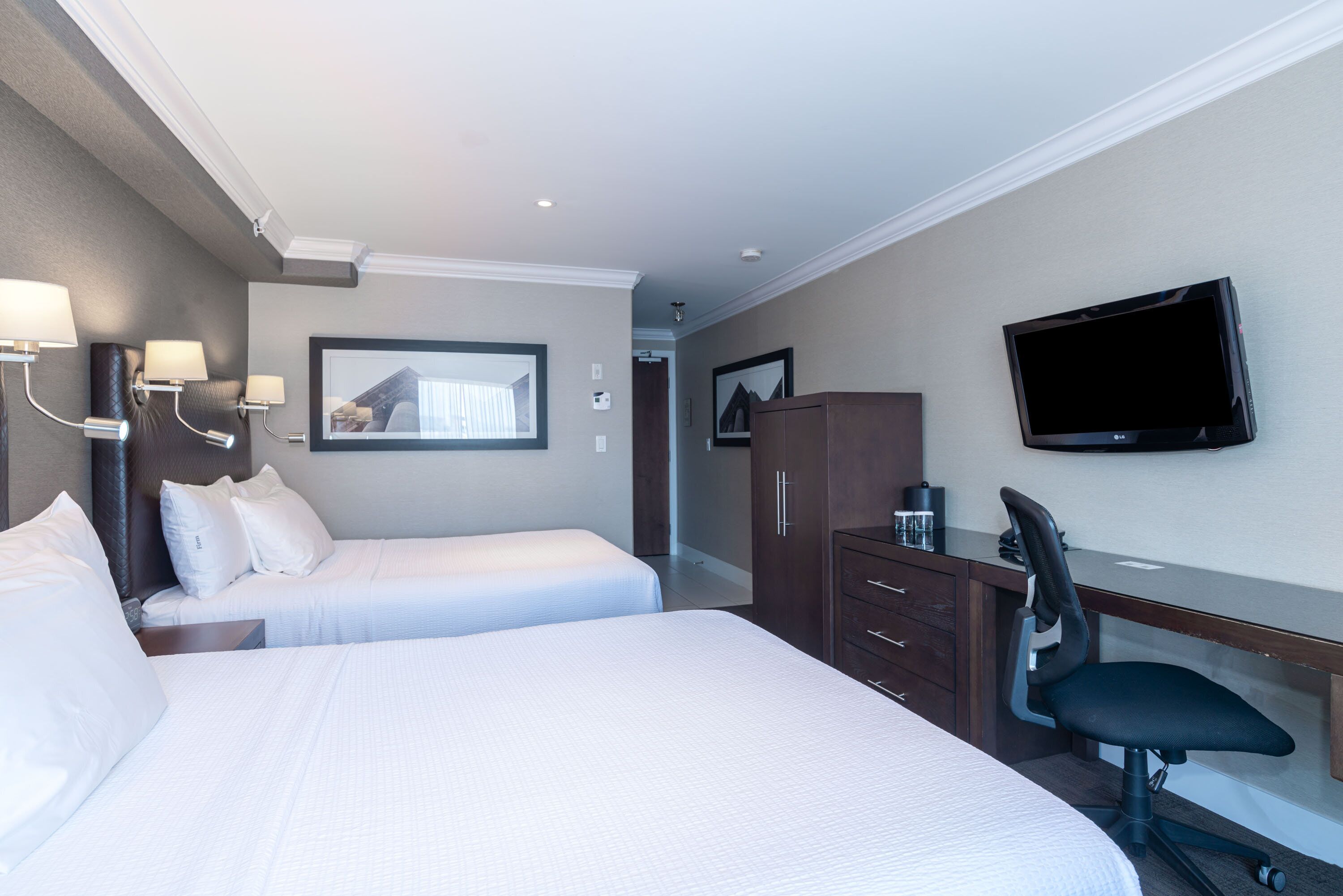 Una habitación de hotel con dos camas, un escritorio, una silla, un televisor y un armario.