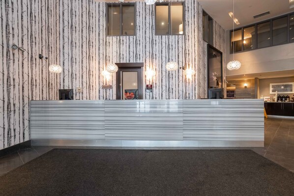 A modern reception area with a patterned wall, a reception desk, and pendant lighting. - Sandman Signature Edmonton South Hotel (Edmonton)