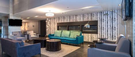 Un salon moderne avec un canapé bleu, des fauteuils gris et un téléviseur à écran plat fixé au mur.