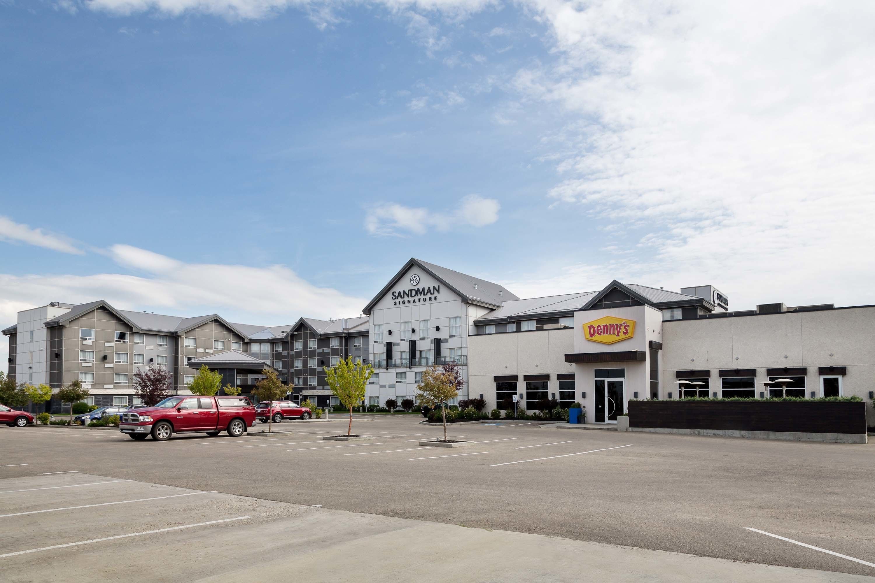 Un parking avec un camion rouge, un bâtiment portant l’enseigne « Signature Sandman » et un restaurant « Denny’s ».