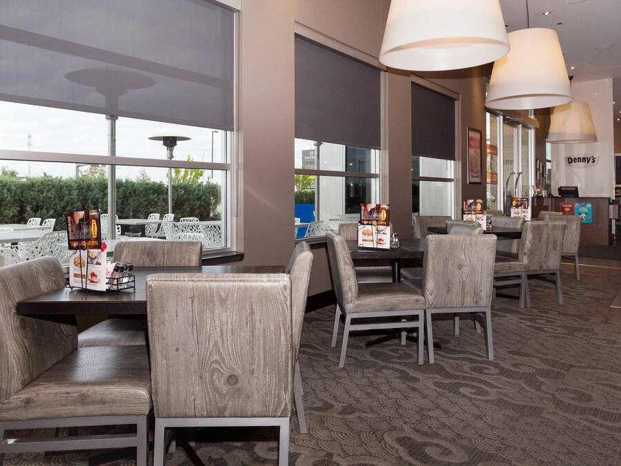 Un restaurante con sillas y mesas de madera, ventanas amplias y lámparas colgantes.